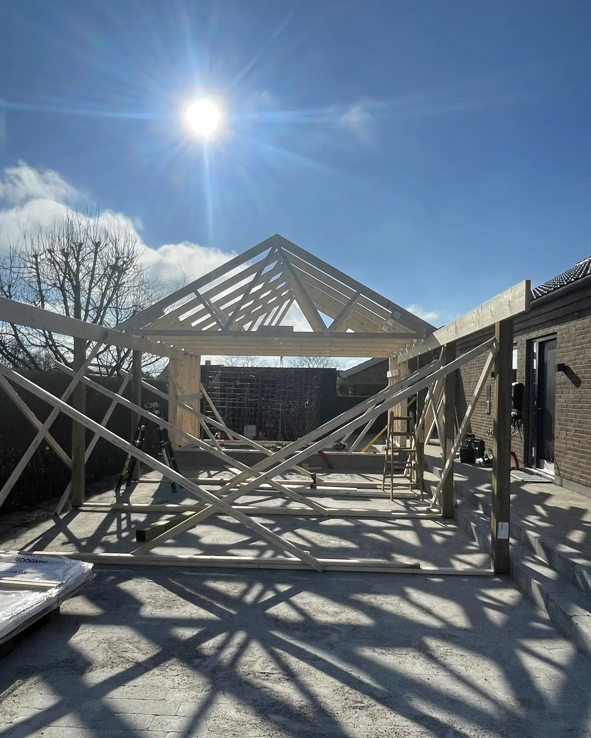 Træskelet med tagspær på stolper, midlertidigt afstivet, mod blå himmel og sol
