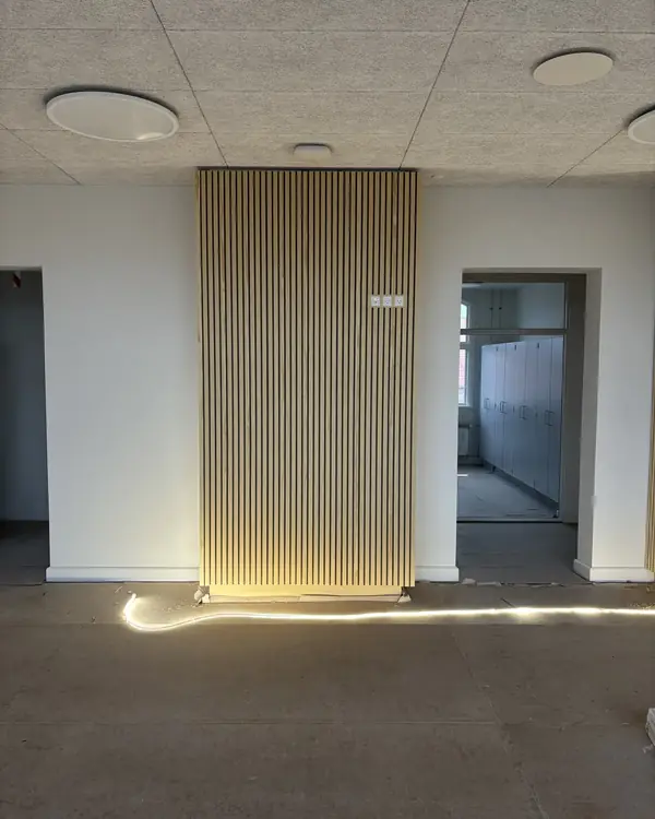Væg beklædt med akustiklameller i træ mellem to døråbninger