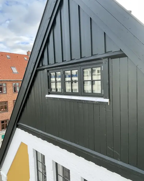 Gavl med mørk lodret træbeklædning og nye vinduer med sprosser og zinksålbænk