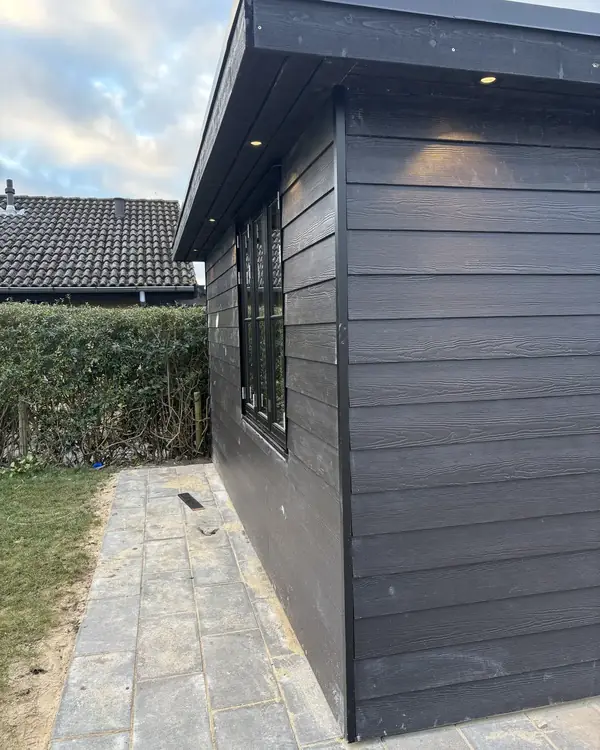 Hjørne af et sort træbeklædt skur med udhæng og indbyggede spots