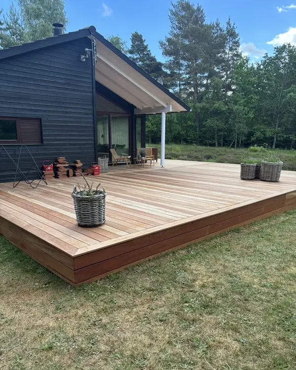 Ny lys træterrasse med sokkel rundt om et sort træbeklædt sommerhus