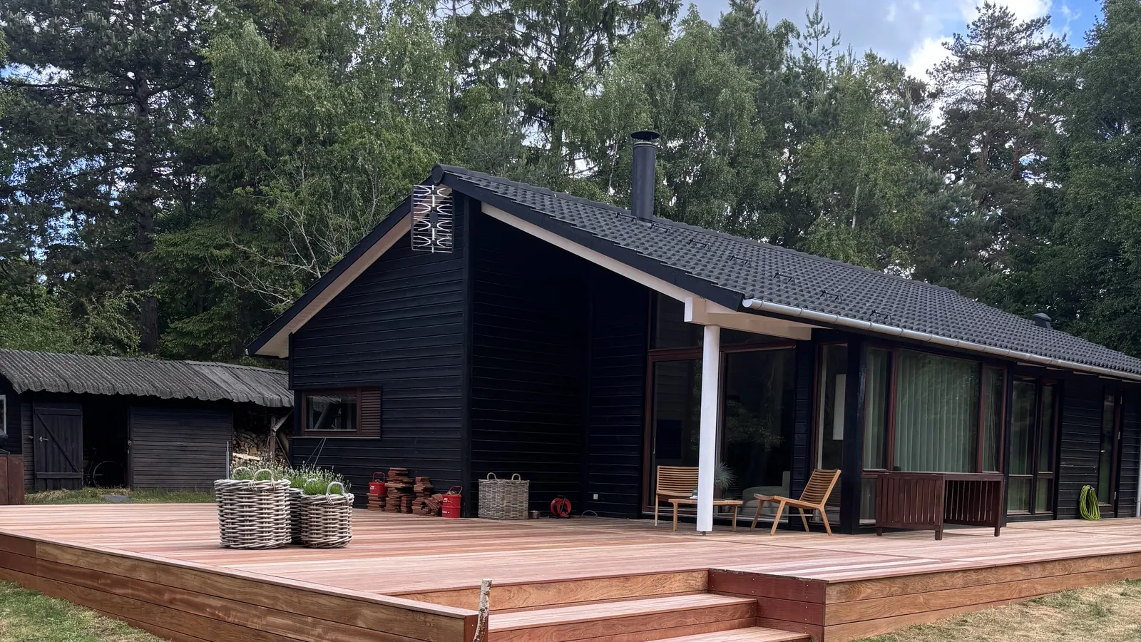 Ny træterrasse med trin rundt om et sort træbeklædt sommerhus